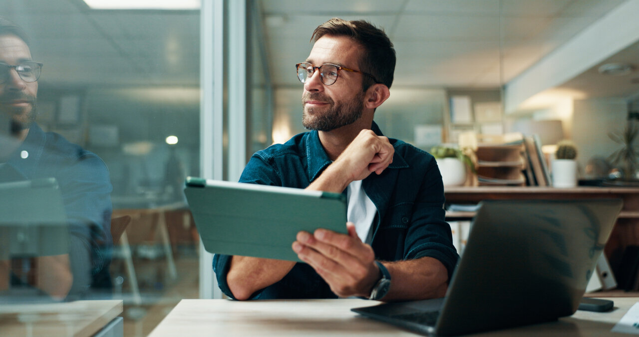 Mann mit Tablet und Laptop an einem Schreibtisch im Büro